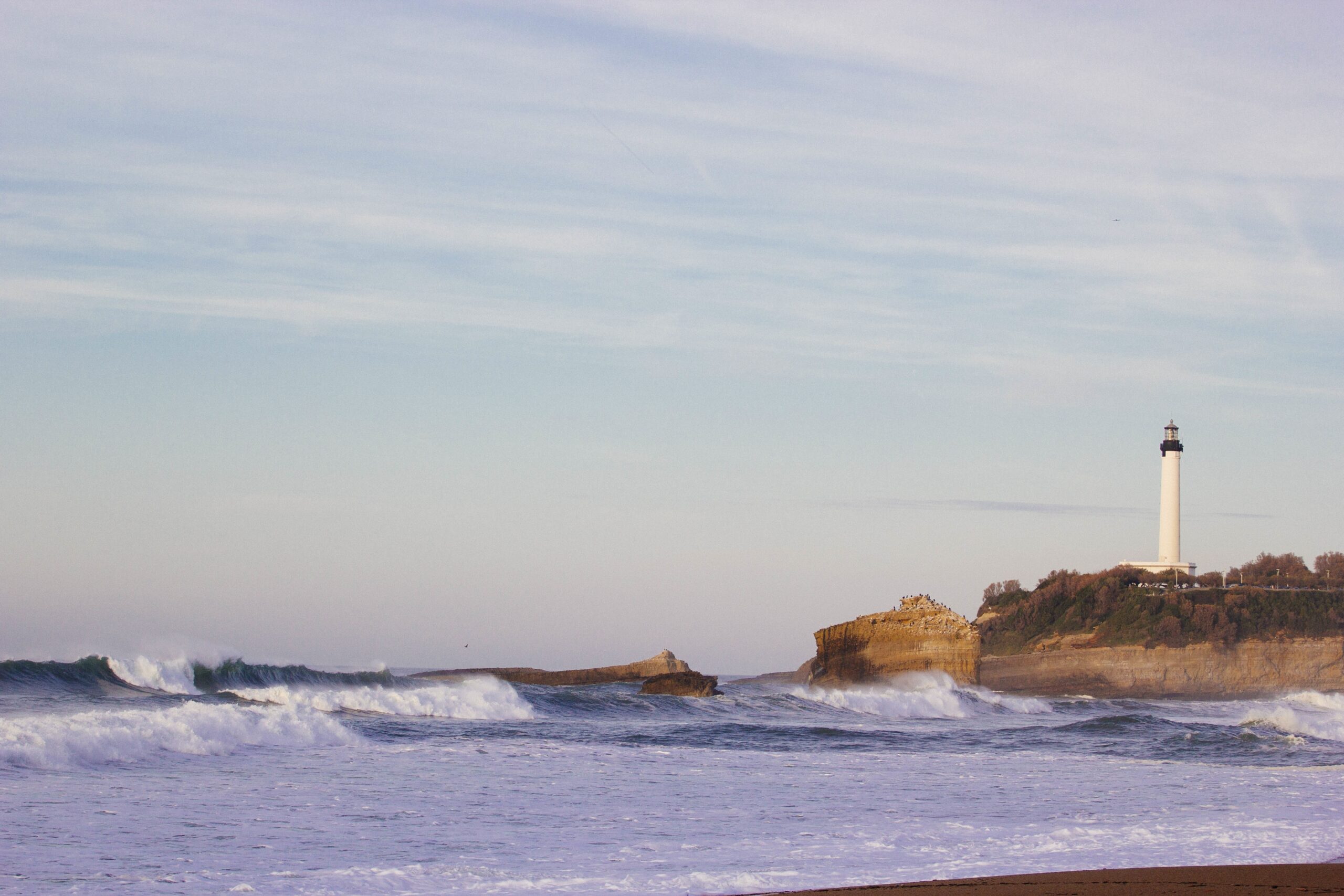 The background is the shoreline along with the sky. Next to the shore, there is a small lighthouse on a cliff.